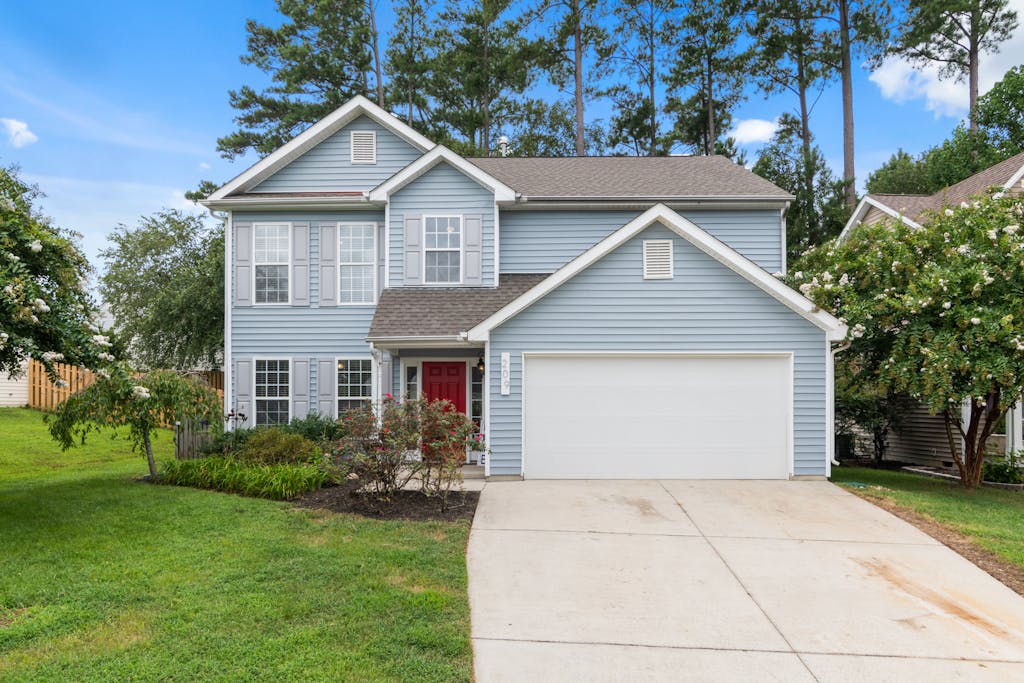 Beautiful suburban home with a red door, driveway, and lush yard.