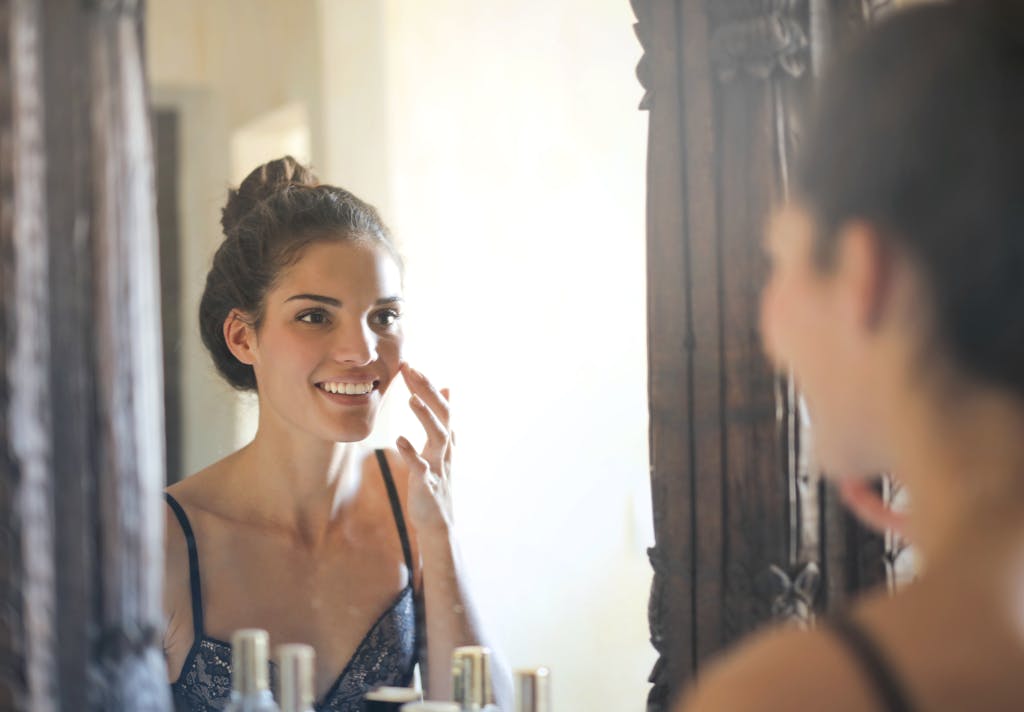 A smiling young woman enjoying her reflection in a room mirror.
