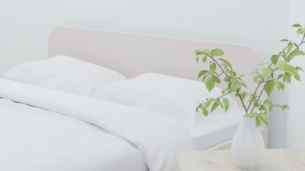 Light and airy modern bedroom with white bedding and a vase of greenery on a wooden table.